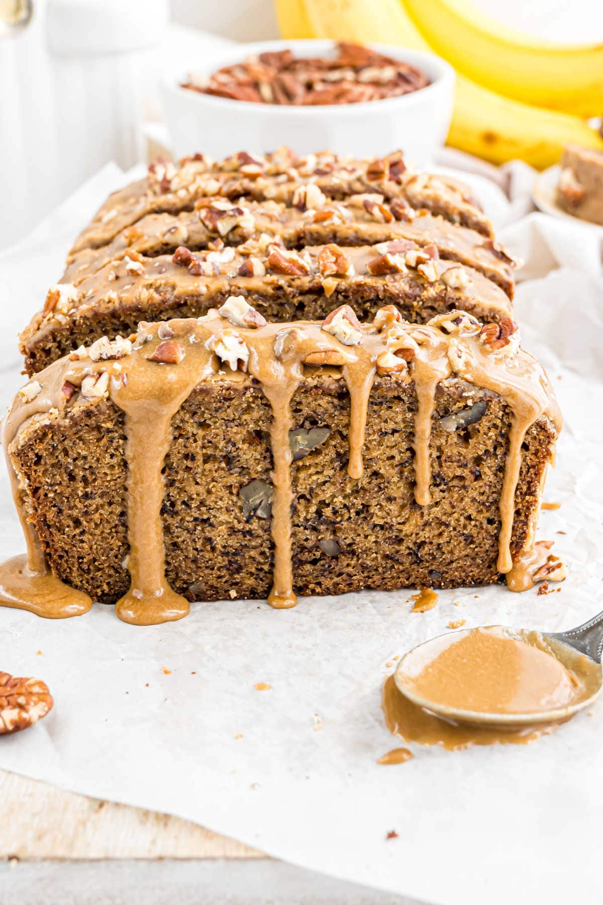 A loaf of maple pecan banana bread topped with icing and chopped pecans, with a spoonful of icing beside it.