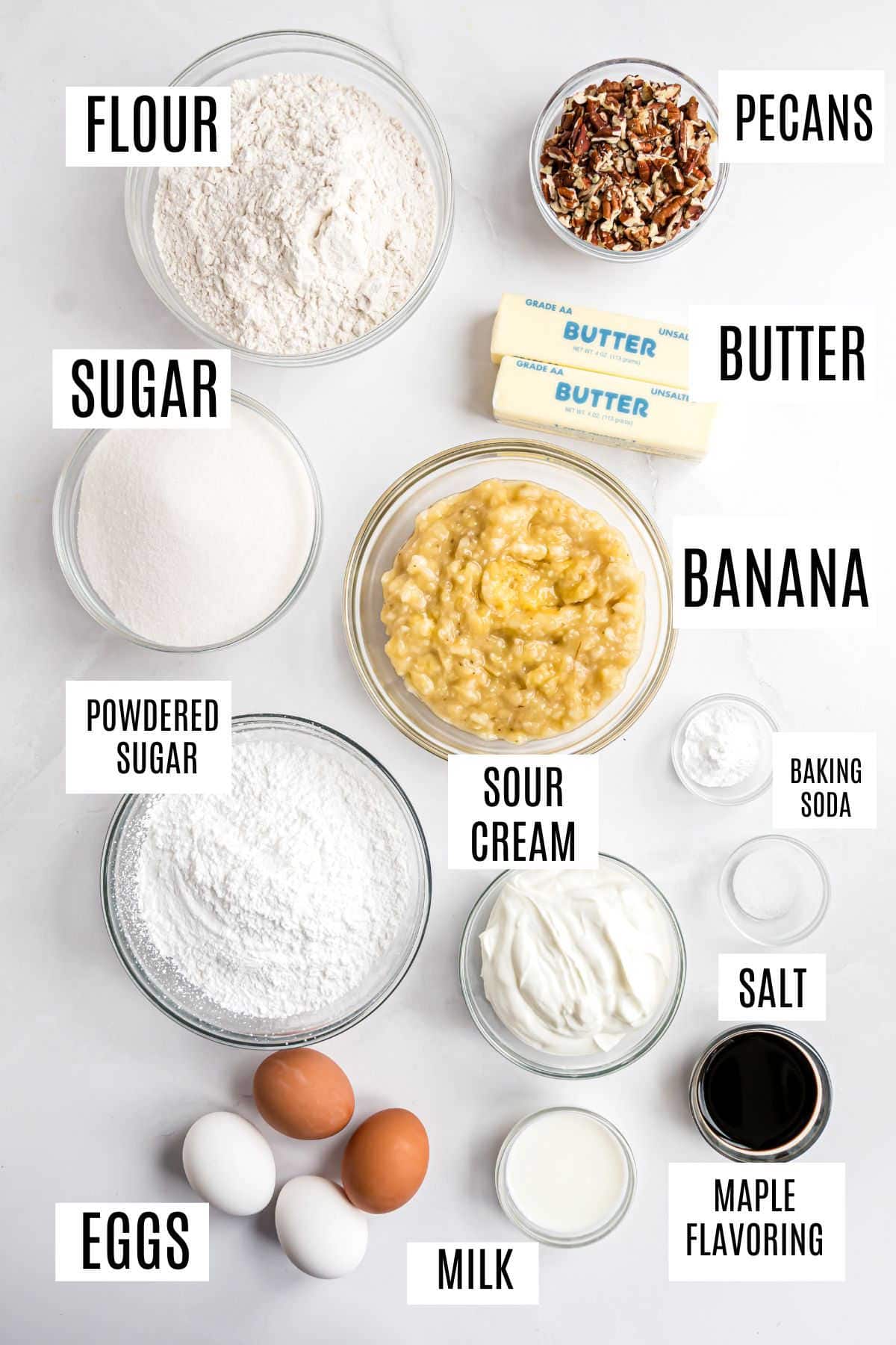 Ingredients for baking maple pecan banana bread: flour, sugar, powdered sugar, eggs, milk, banana, sour cream, butter, pecans, salt, and more.