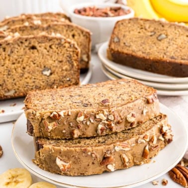 Two slices of maple pecan banana bread with chopped pecans on top, with more sliced bread in the background.
