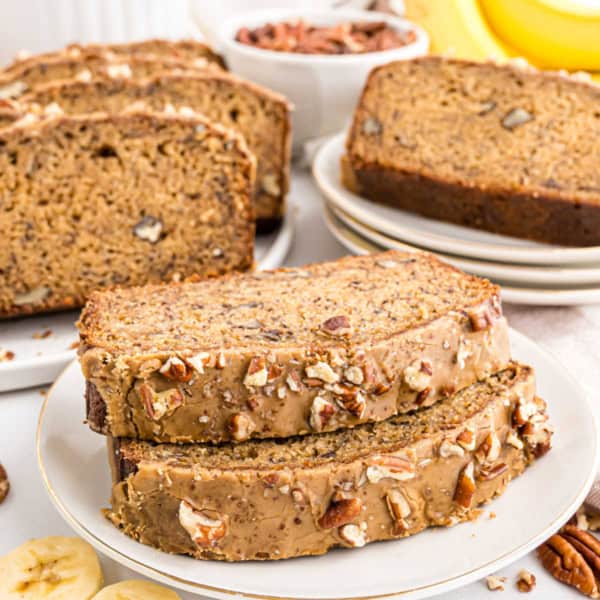 Two slices of maple pecan banana bread with chopped pecans on top, with more sliced bread in the background.