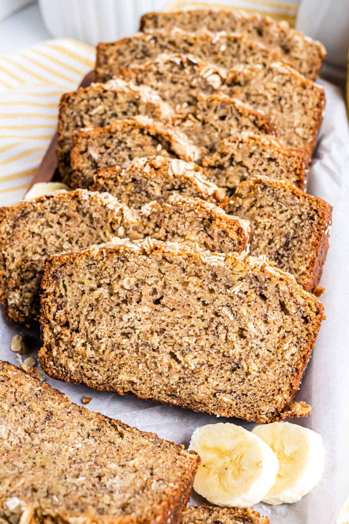 Sliced oatmeal banana bread on parchment paper with banana slices beside it.