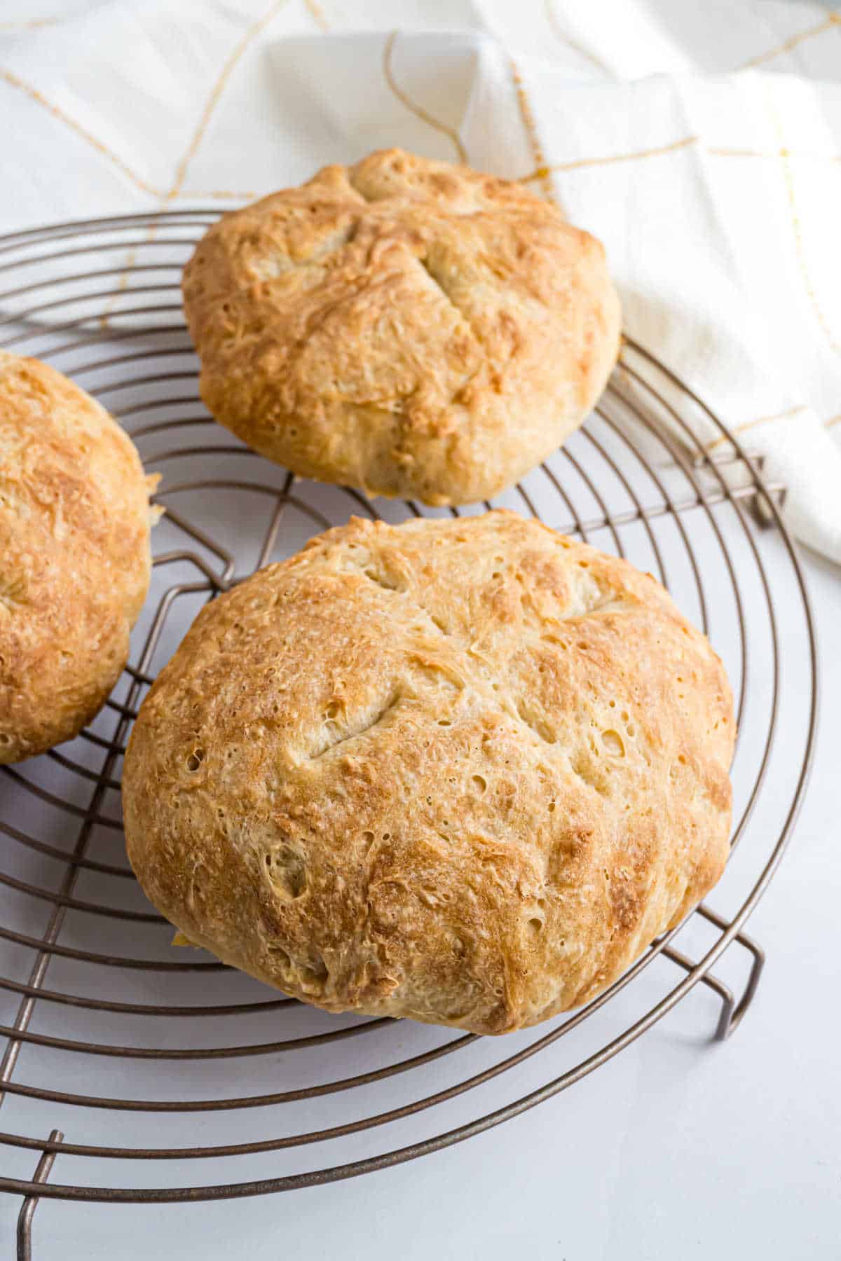 Two round bread bowls with a golden brown crust cool on a metal rack, a white towel in the background adding a cozy touch.