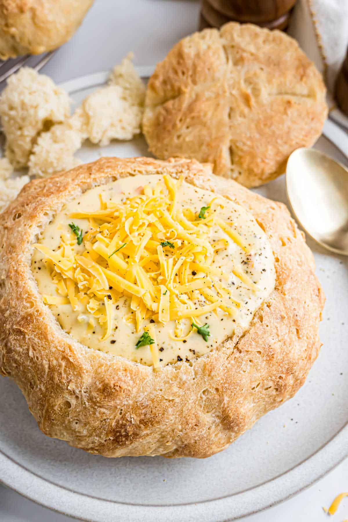 Cheese soup served in a bread bowl, topped with shredded cheese and herbs, with extra bread pieces on the side—perfect for fans of hearty bread bowls.