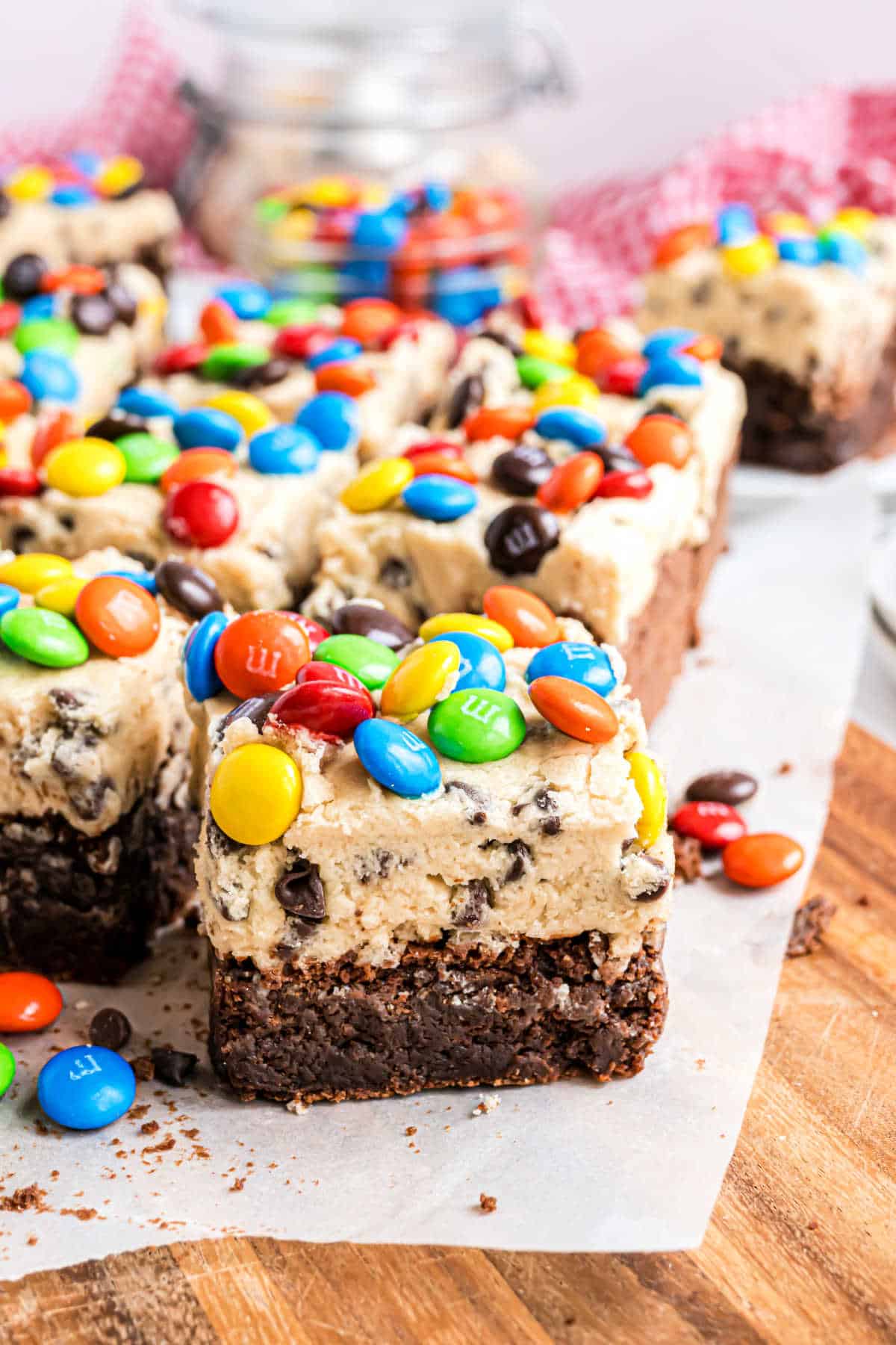Brownie squares topped with cookie dough and colorful M&M candies, arranged on parchment paper.