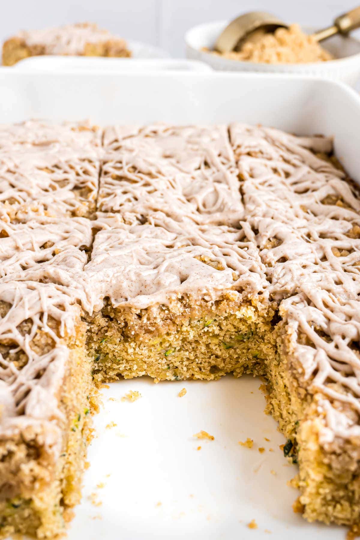 Sliced iced coffee cake in a white baking dish with one piece missing, showing the moist interior.