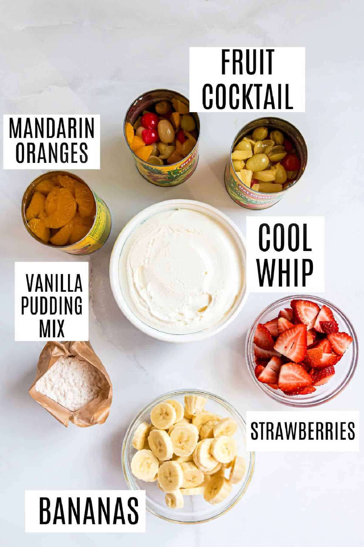 Overhead view of labeled ingredients: fruit cocktail, mandarin oranges, Cool Whip, vanilla pudding, strawberries, bananas.