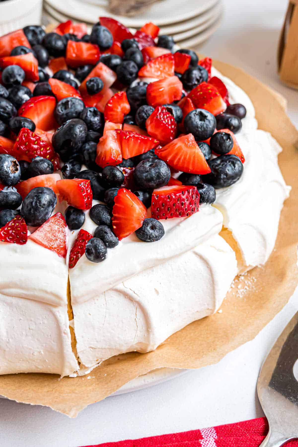 A pavlova topped with whipped cream, fresh strawberries, and blueberries, sliced and ready to serve.