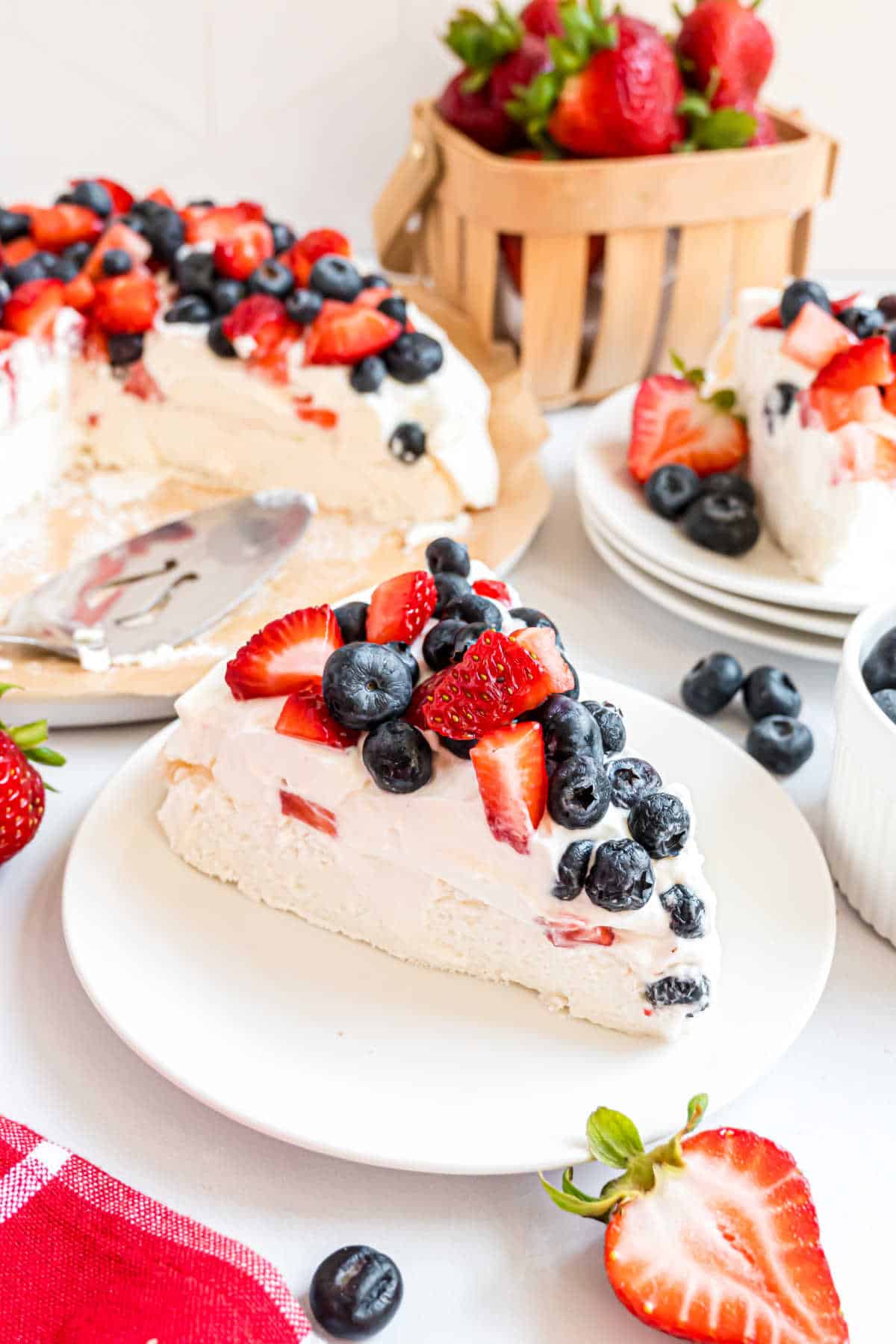 A slice of berry-topped cheesecake on a plate, with strawberries and blueberries scattered around.
