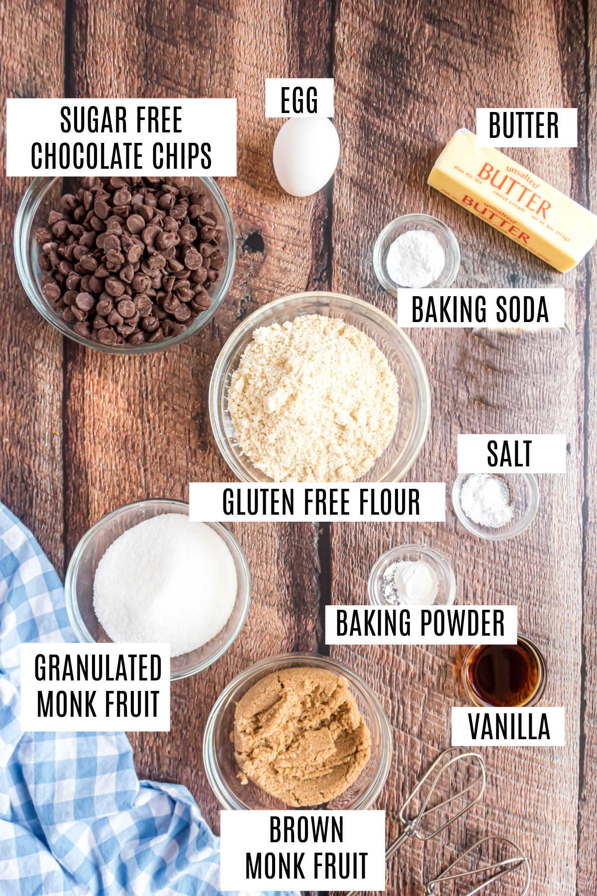 Bowls of labeled ingredients for baking sugar free chocolate chip cookies, including chocolate chips, flours, sweeteners, butter, and egg.