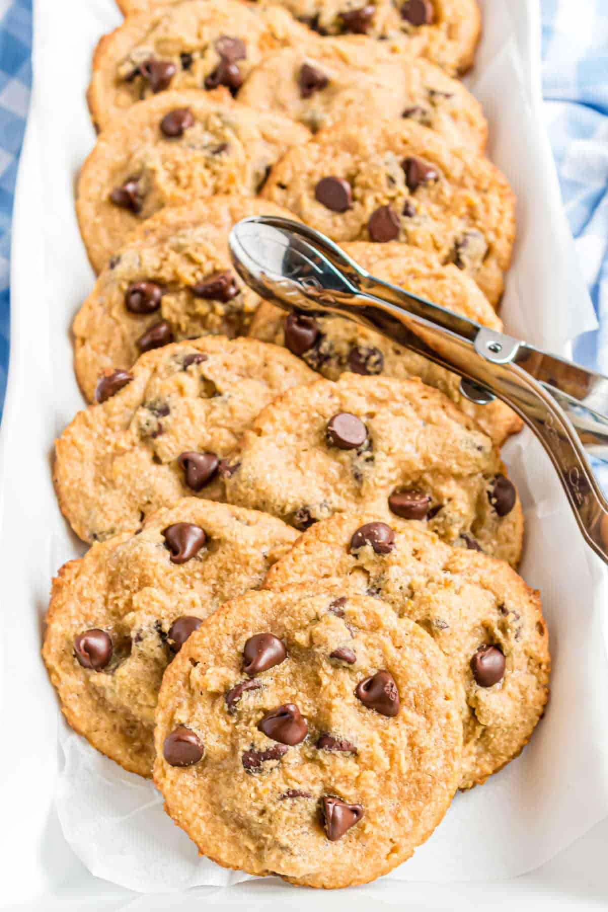 A tray of chocolate chip cookies with a metal scoop, arranged on white parchment paper.