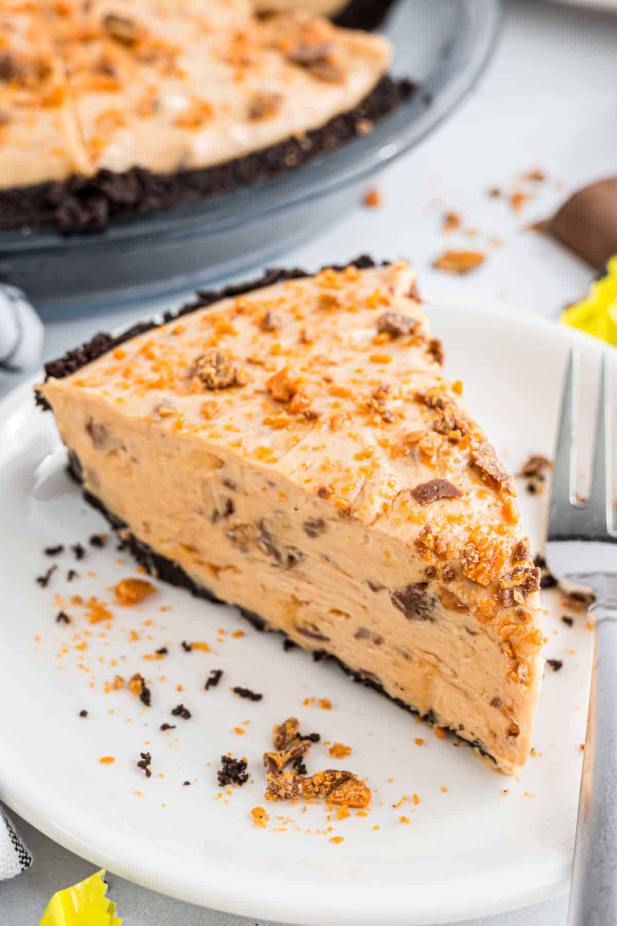 A slice of creamy peanut butter pie with crushed candy on top, served on a white plate with a fork.