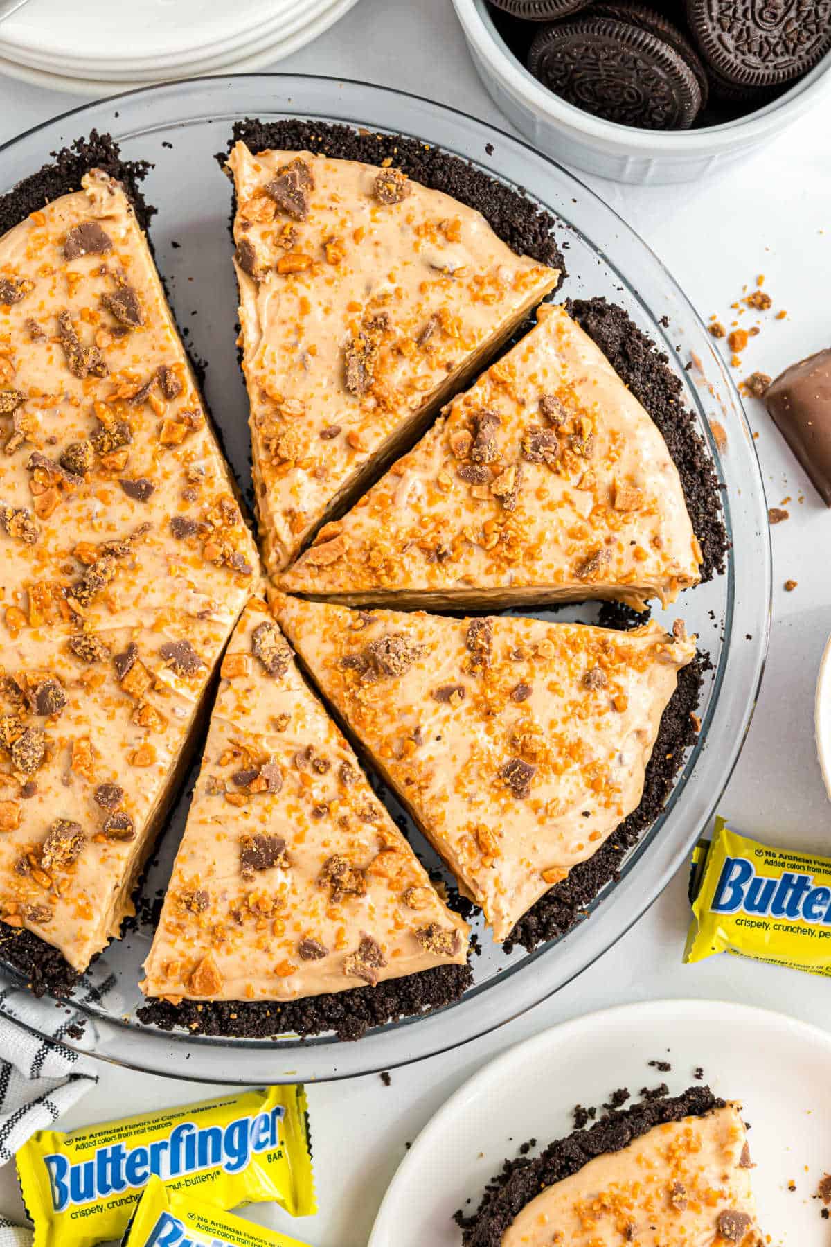 A Butterfinger pie with an Oreo crust, sliced and topped with crushed Butterfinger candy bars.