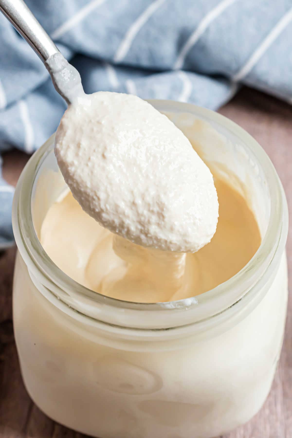 A spoonful of thick, creamy yogurt is being lifted from a glass jar.