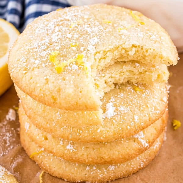 A stack of lemon cookies topped with powdered sugar, with a bite taken from the top cookie.