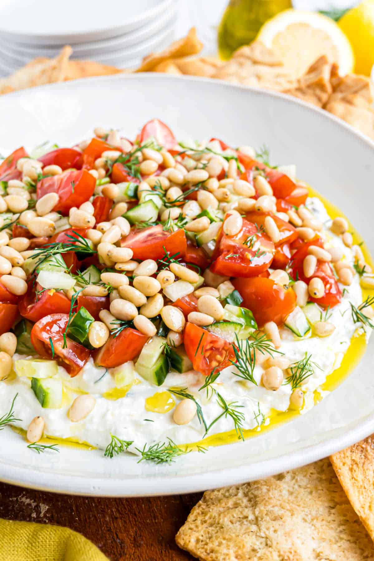A plate of whipped feta dip topped with chopped tomatoes, cucumbers, pine nuts, and fresh dill.