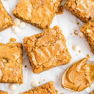Blondie bars with crackled tops, white chocolate chips, and a spoonful of creamy peanut butter on parchment paper.