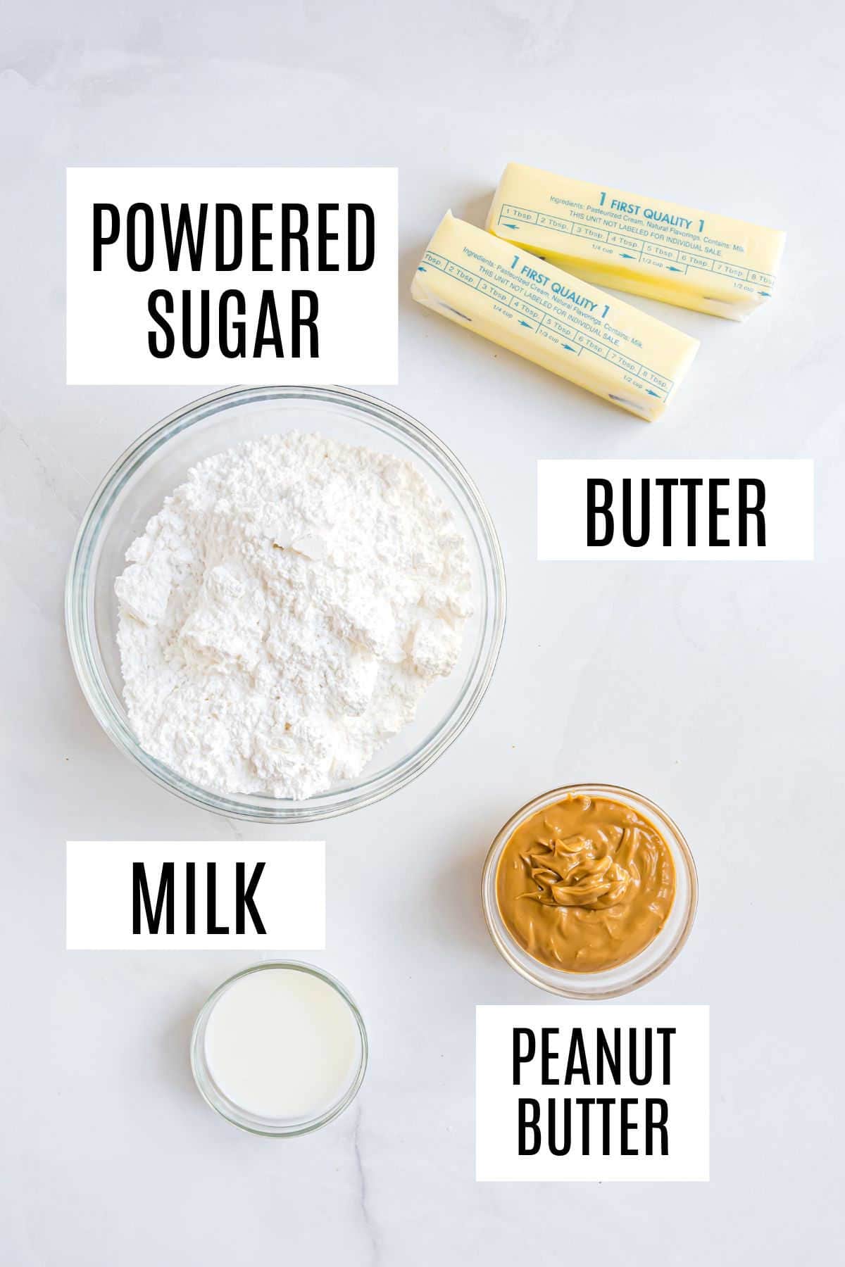 Powdered sugar, butter sticks, milk, and peanut butter in bowls on a white surface, each labeled.