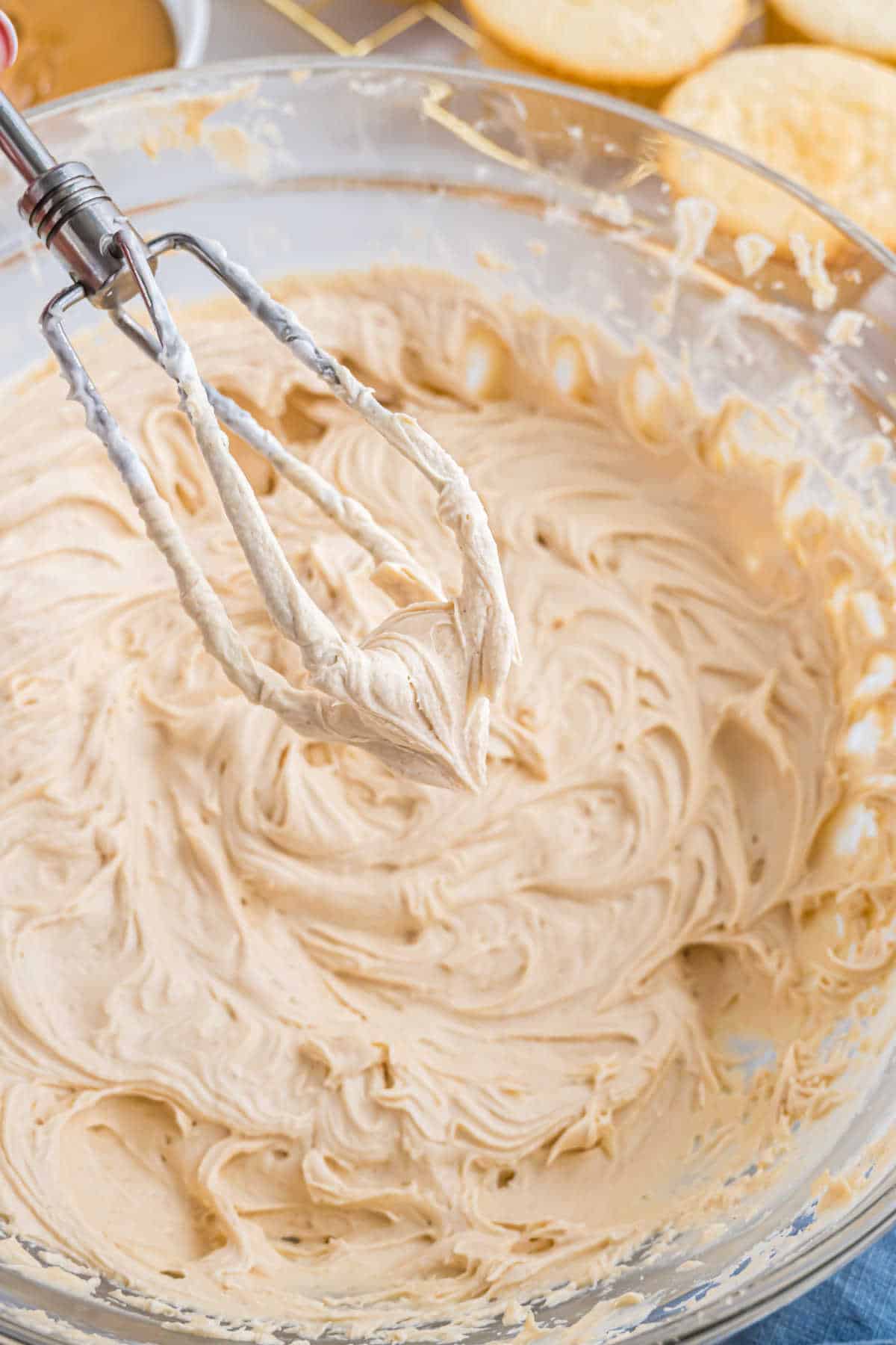Close-up of a mixing bowl with creamy, light brown batter and a hand mixer with batter on its beaters.