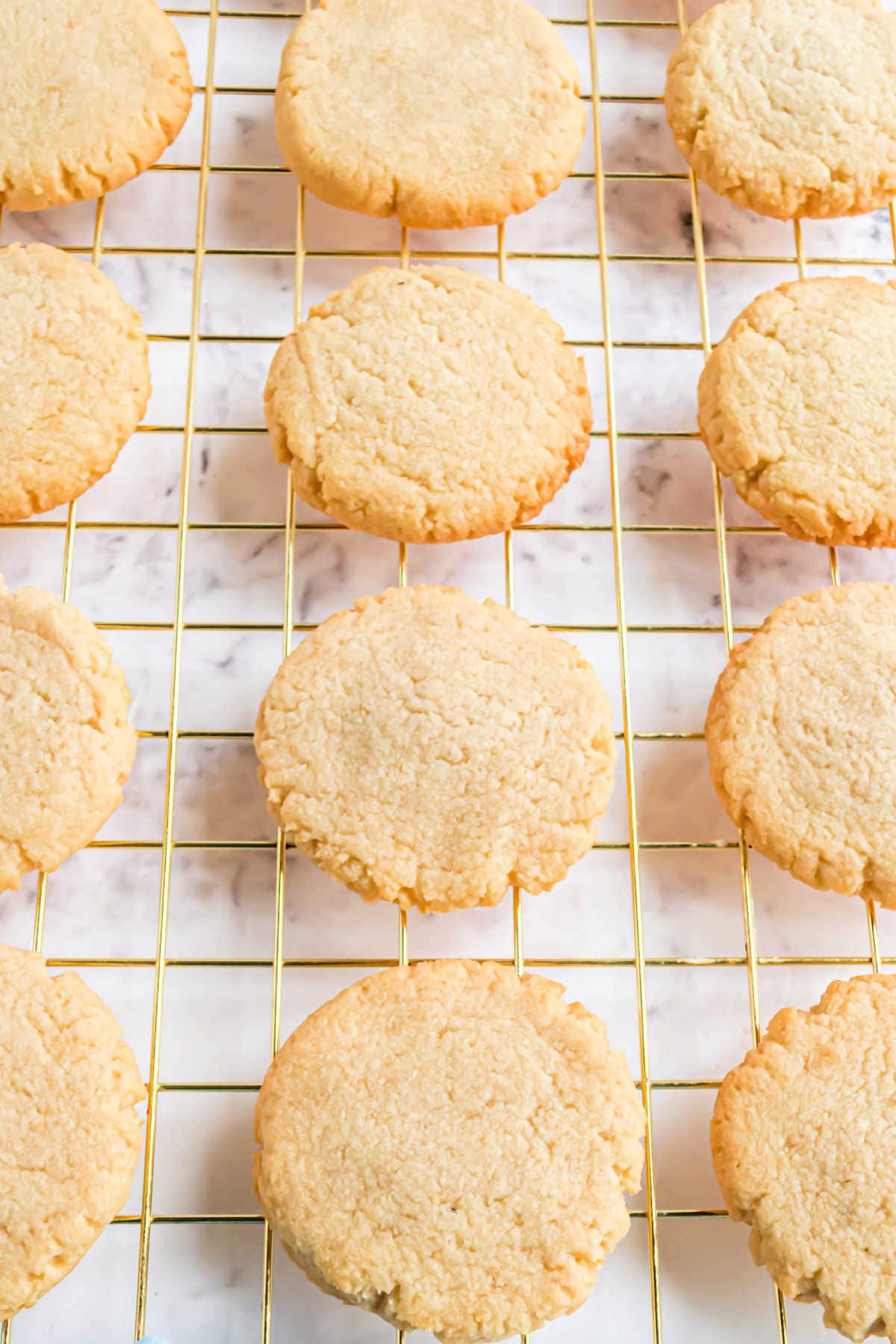 Round, golden shortbread cookies cooling on a wire rack over a marble surface.