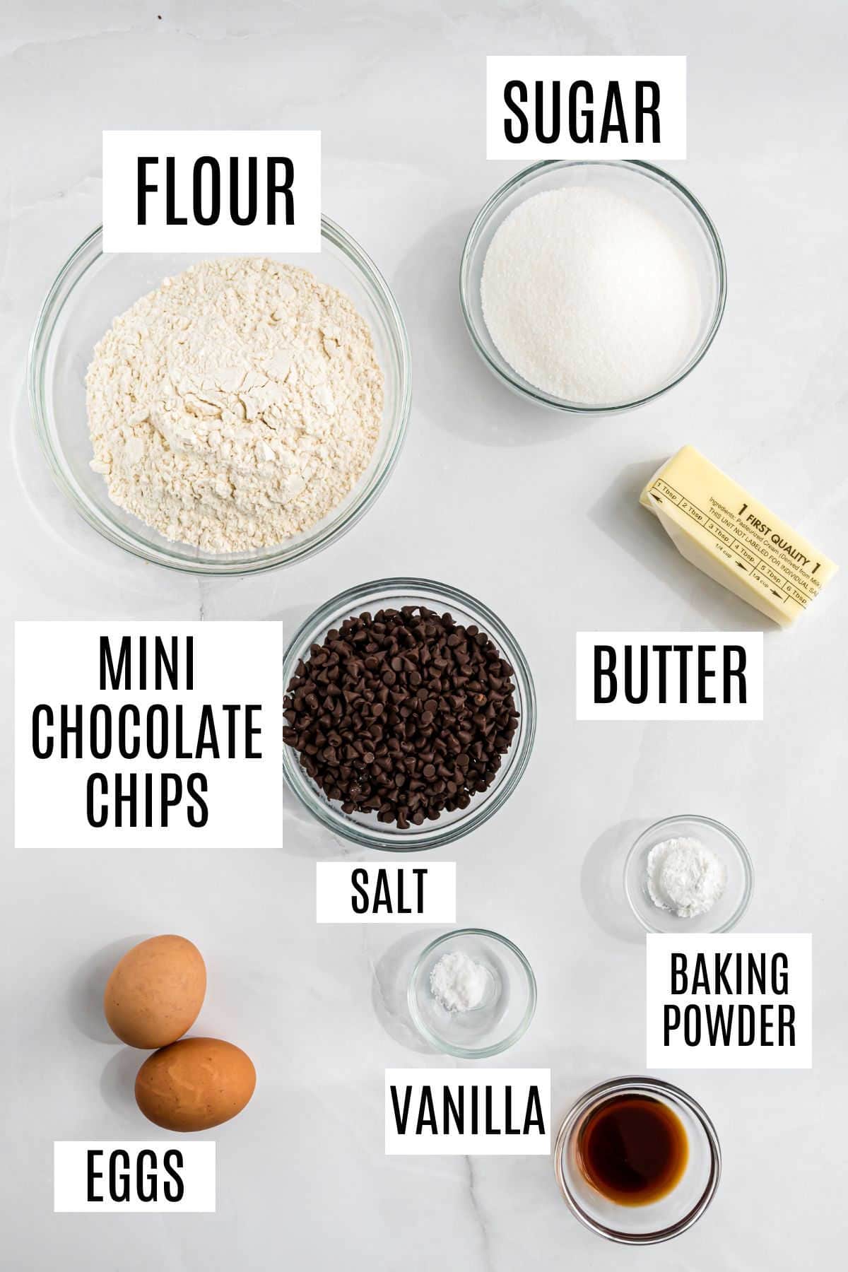 Baking ingredients: flour, sugar, butter, eggs, mini chocolate chips, salt, vanilla, and baking powder in bowls.