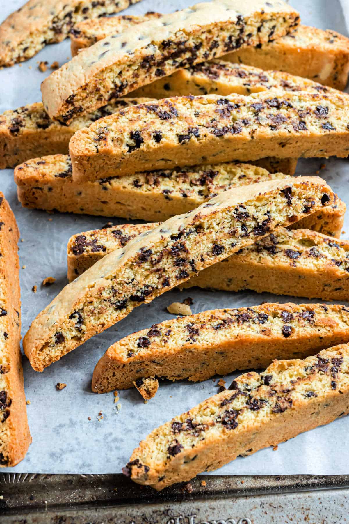 A pile of chocolate chip biscotti on parchment paper, showing their crunchy texture and golden color.