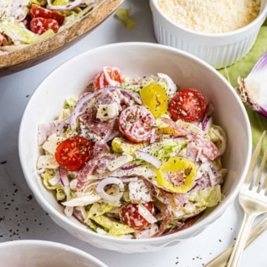 A bowl of Italian chopped salad with lettuce, tomatoes, red onions, salami, cheese, and banana peppers.