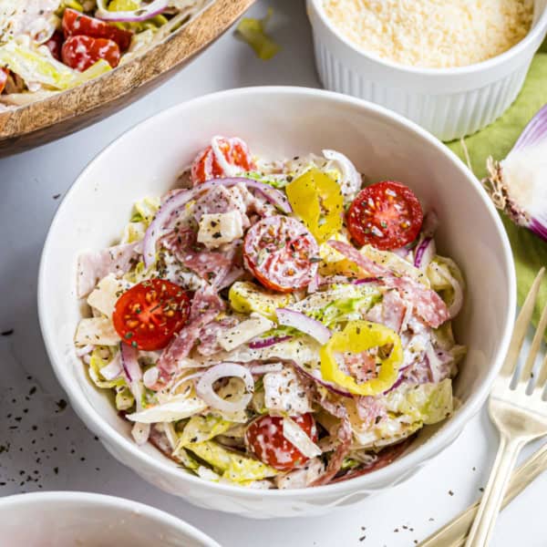 A bowl of Italian chopped salad with lettuce, tomatoes, red onions, salami, cheese, and banana peppers.