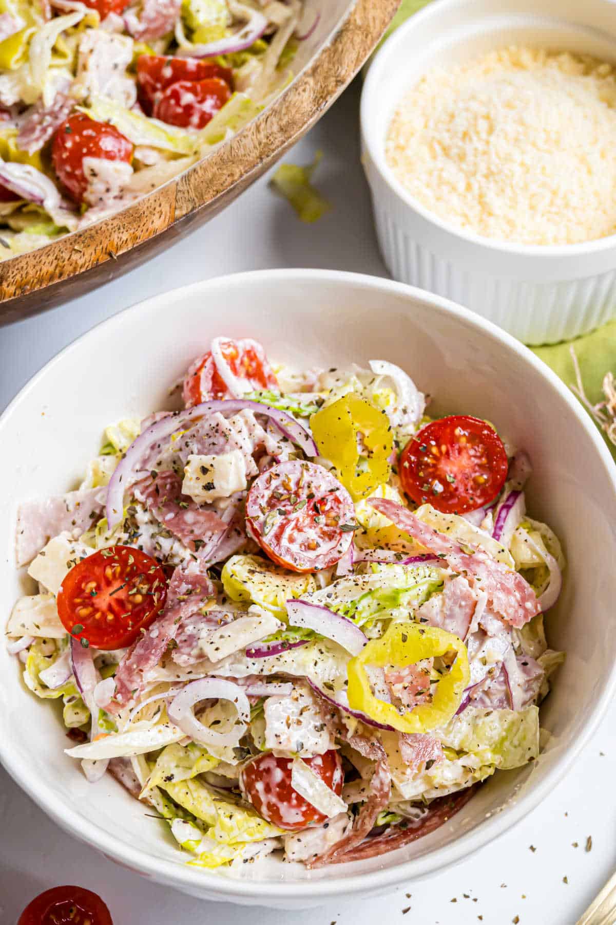 Bowl of Italian chopped salad with lettuce, cherry tomatoes, salami, onions, and creamy dressing.