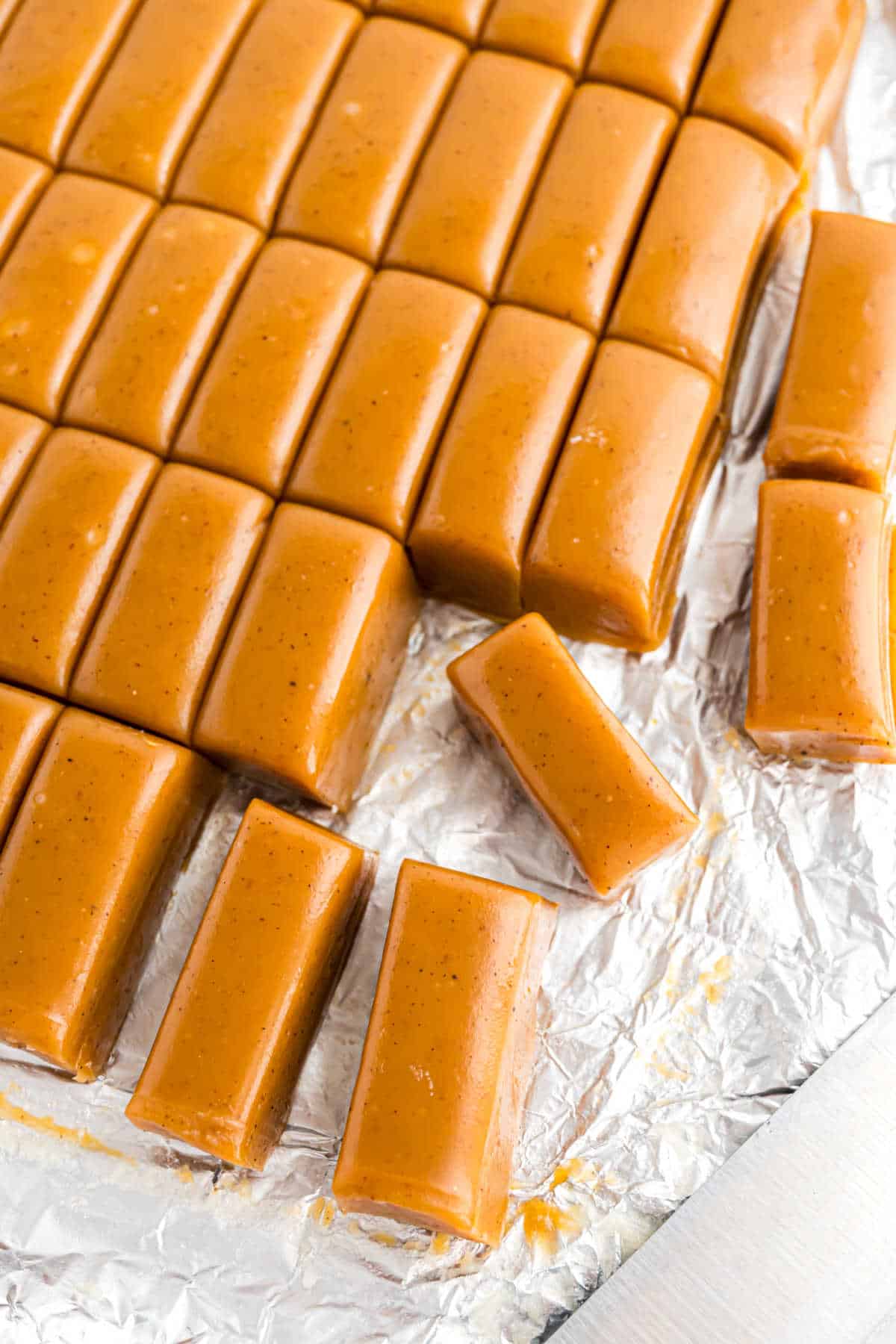 Caramel candies cut into rectangles and arranged on foil-covered surface.