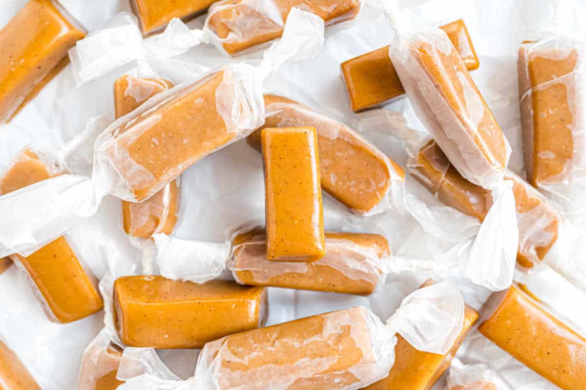 Wrapped caramel candies scattered on a white surface, each piece in clear wax paper.