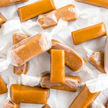 Caramel candies wrapped in clear wax paper scattered on a white surface.