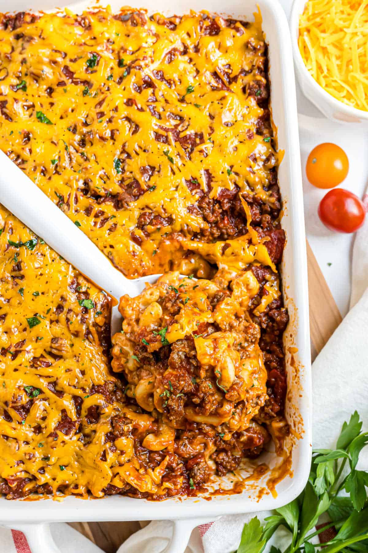 A casserole dish of cheesy beef and macaroni with a serving spoon scooping out a portion.
