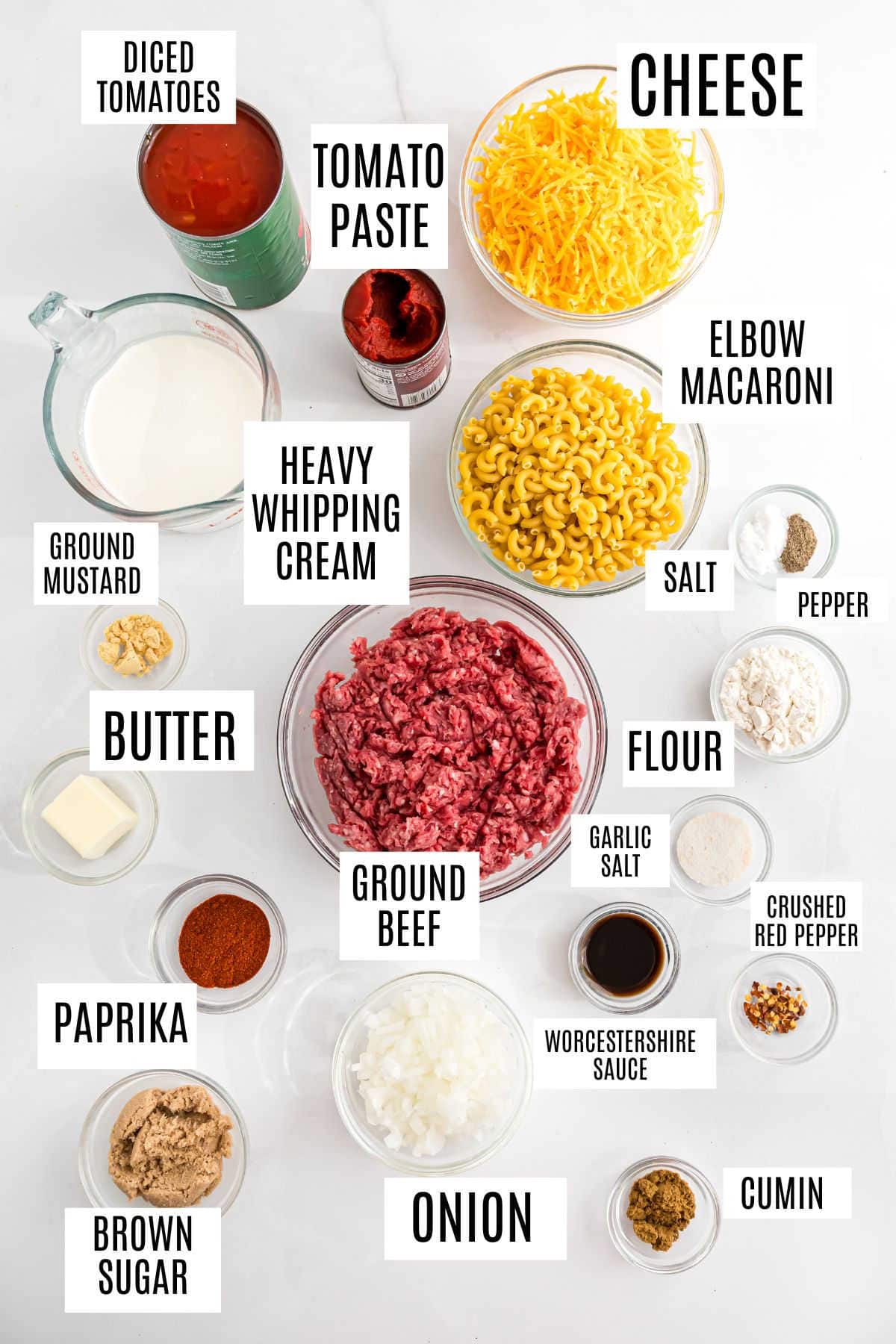 Ingredients for cheeseburger macaroni laid out in bowls, labeled, on a white surface.