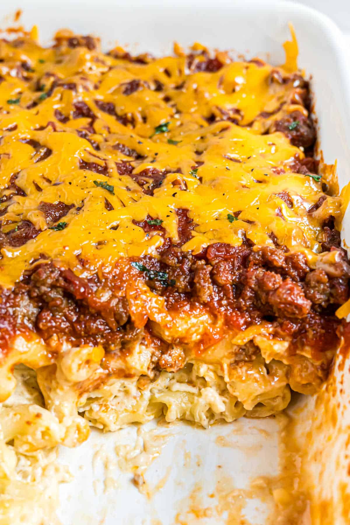 A cheesy beef casserole with a slice removed, showing layers of noodles, meat sauce, and melted cheddar cheese.