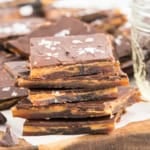 Chocolate toffee bark pieces stacked on a wooden board, topped with flaky sea salt.