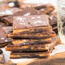 Chocolate toffee bark pieces stacked on a wooden board, topped with flaky sea salt.