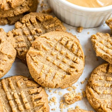 Peanut butter cookies with a crisscross pattern next to a bowl of creamy peanut butter.