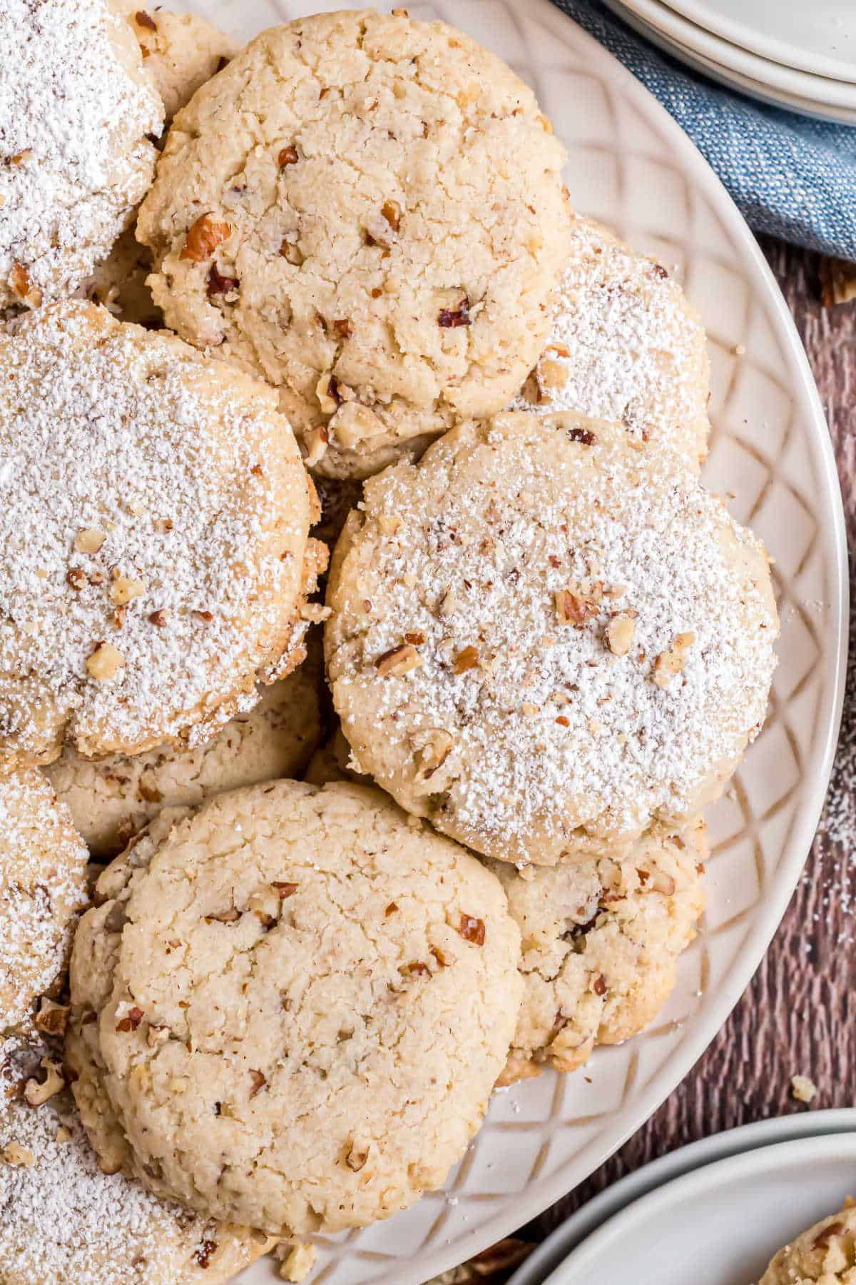 Close-up of pecan cookies topped with powdered sugar, arranged on a patterned white plate.