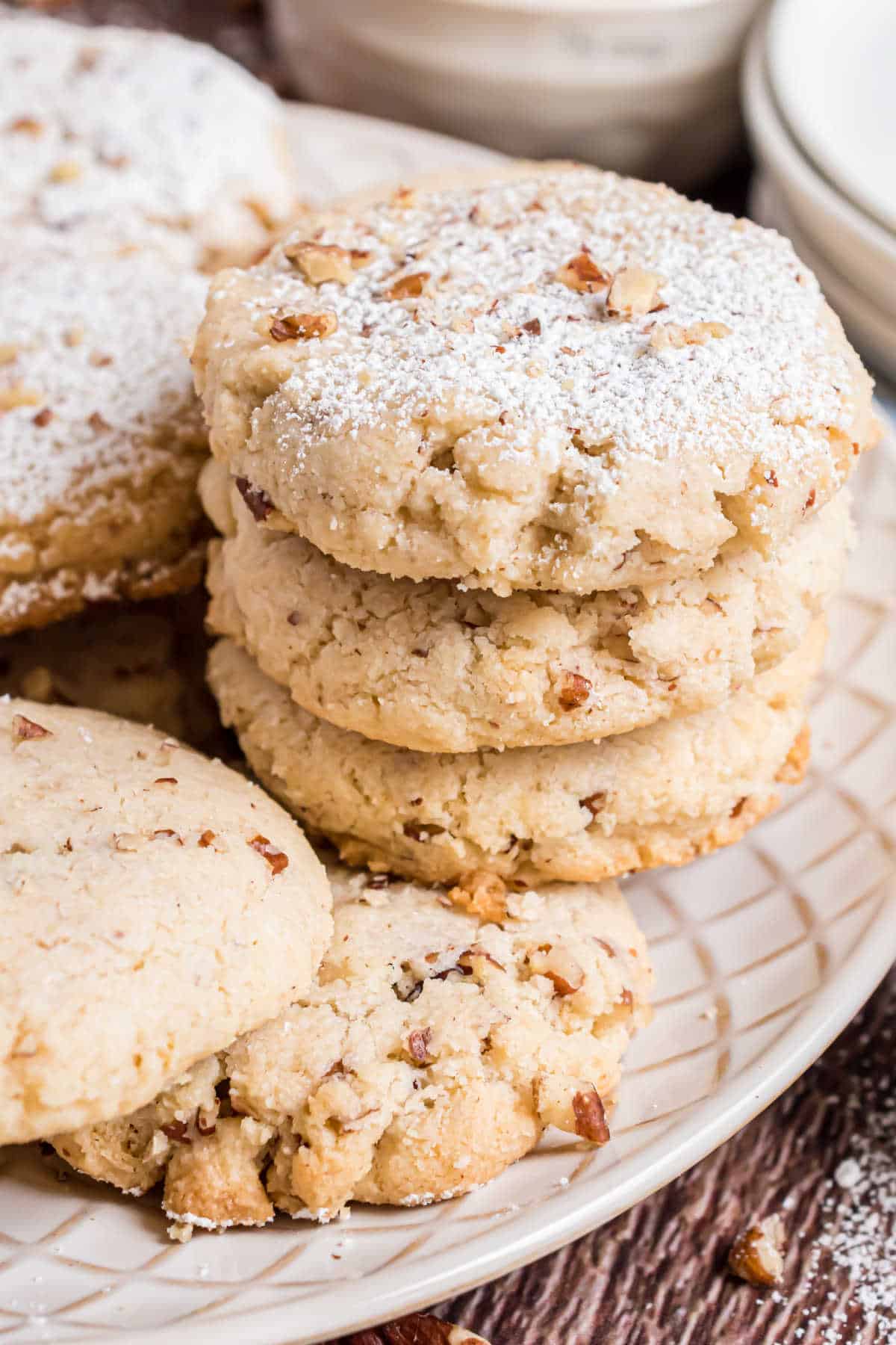 A stack of powdered sugar-dusted cookies with chopped nuts on a white plate.