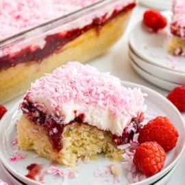 A slice of raspberry coconut cake with pink coconut topping, served on a plate with fresh raspberries.