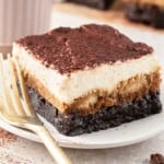 A slice of tiramisu brownie on a plate with a gold fork, topped with cocoa powder.
