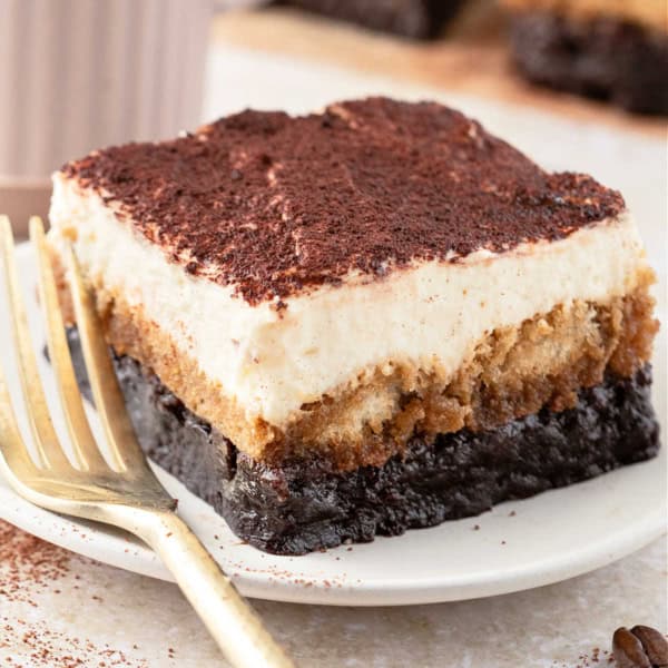 A slice of tiramisu brownie on a plate with a gold fork, topped with cocoa powder.