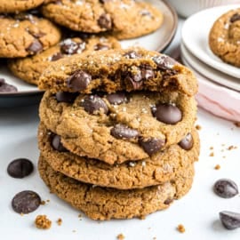 Three chocolate chip cookies stacked, topped with sea salt, with one broken in half on top.