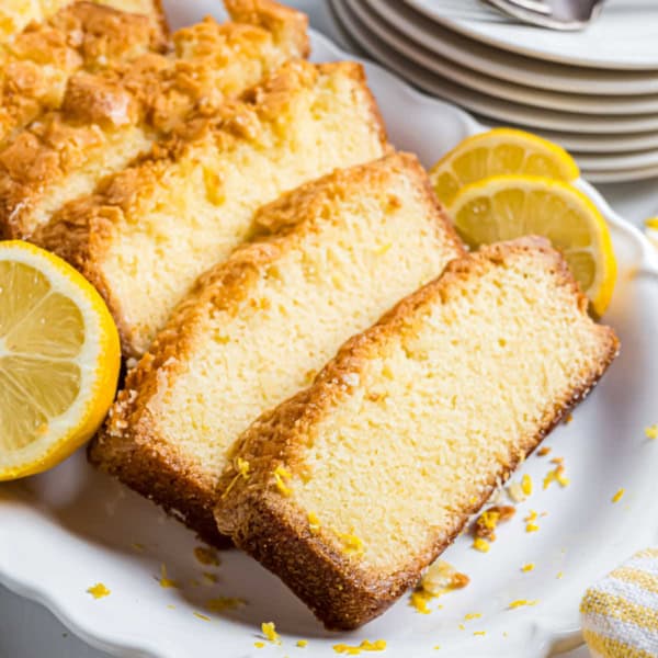 Sliced lemon pound cake on a white plate, garnished with lemon slices and zest.