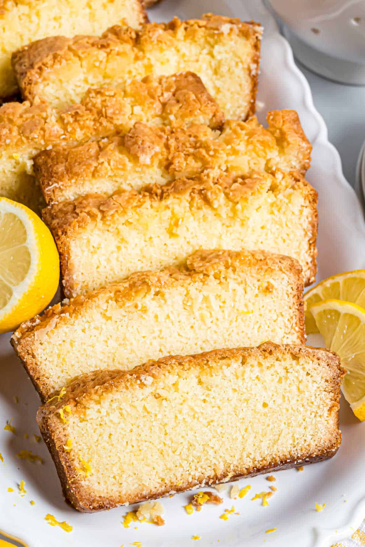 Slices of lemon bread arranged on a white plate with lemon wedges on the side.