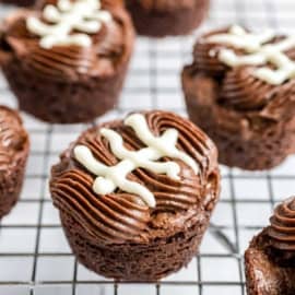 Chocolate cupcakes with piped frosting and white icing shaped like football laces, on a wire cooling rack.