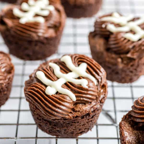 Chocolate cupcakes with piped frosting and white icing shaped like football laces, on a wire cooling rack.