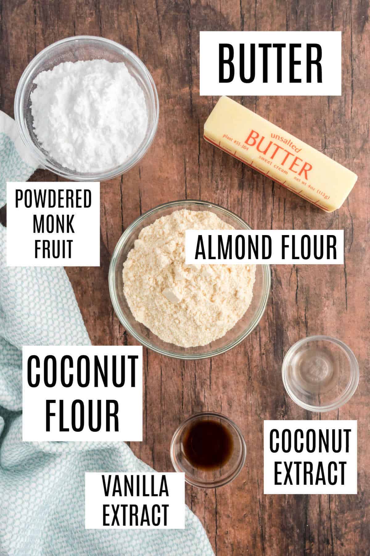 Top-down view of labeled baking ingredients: butter, almond flour, coconut flour, powdered monk fruit, extracts.