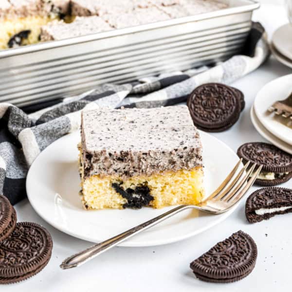 A slice of cookies and cream cake on a plate with a fork, surrounded by chocolate sandwich cookies.