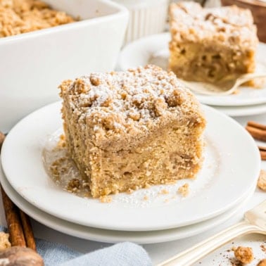 A slice of crumb-topped coffee cake dusted with powdered sugar on a white plate.